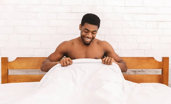 Excited african-american man looking at his body part under sheets — Stock Photo, Image