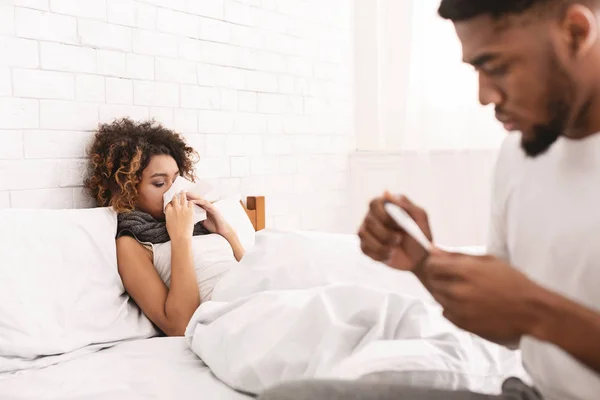 Больная женщина в постели, мужчина проверяет температуру на термометре — стоковое фото