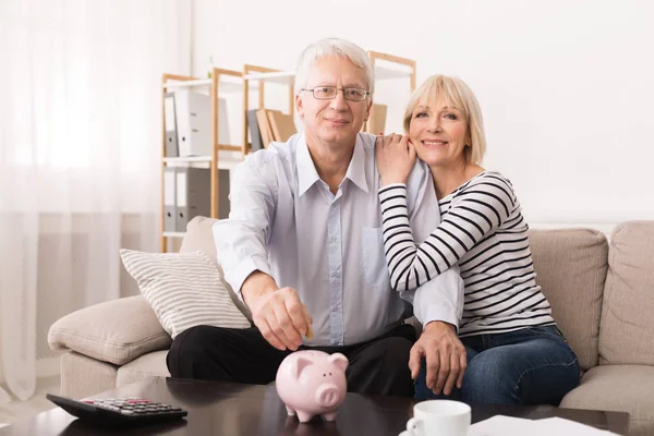 Elderly couple saving money in piggybank at home
