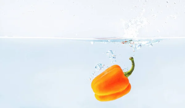 Paprika arancione colorata in spruzzi d'acqua su sfondo blu — Foto Stock