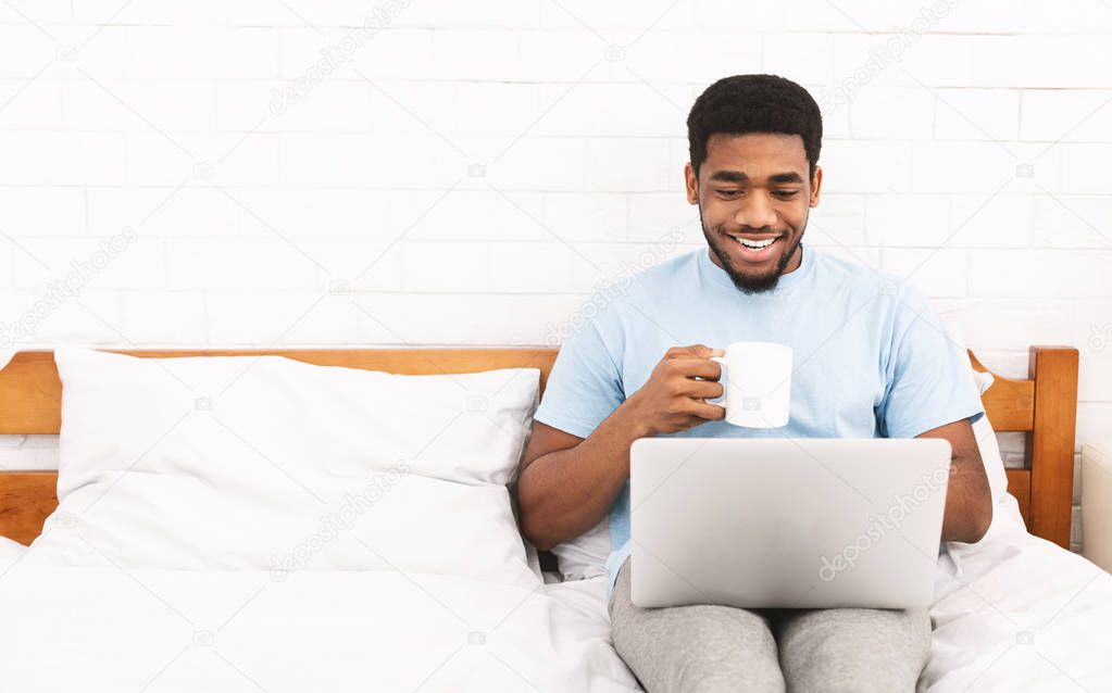 Young millennial guy using laptop in bed