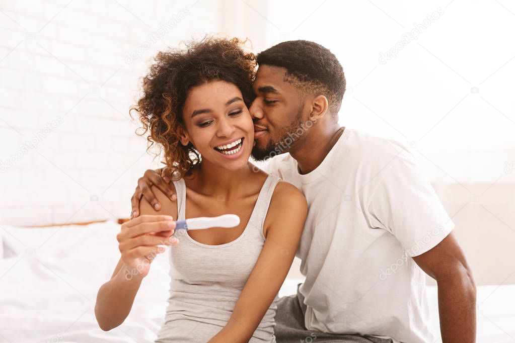 Happy couple holding positive pregnancy test on bed