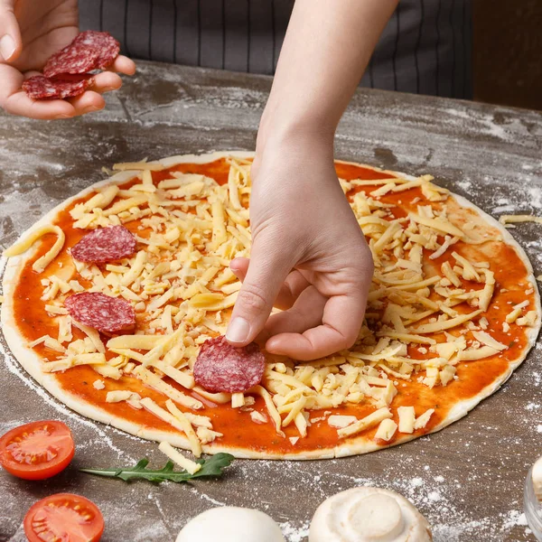 Frau bereitet hausgemachte Pizza zu, fügt Salami hinzu, Nahaufnahme — Stockfoto
