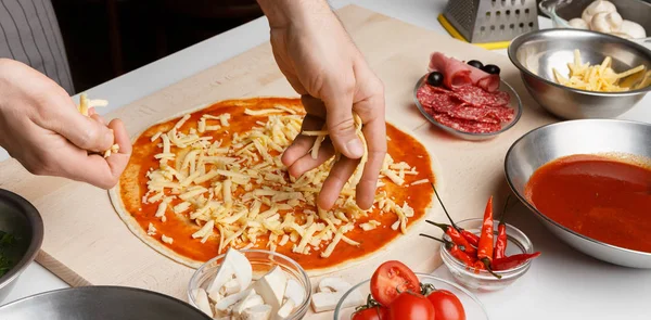 Koch bestreut Pizza mit Käse in Küche — Stockfoto