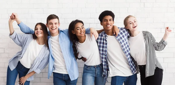 Разнообразные подростки обнимаются и веселятся над белой стеной — стоковое фото