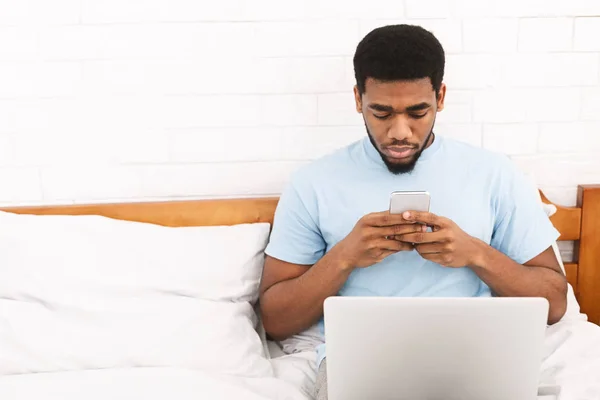 Joven en pijama usando celular en la cama — Foto de Stock