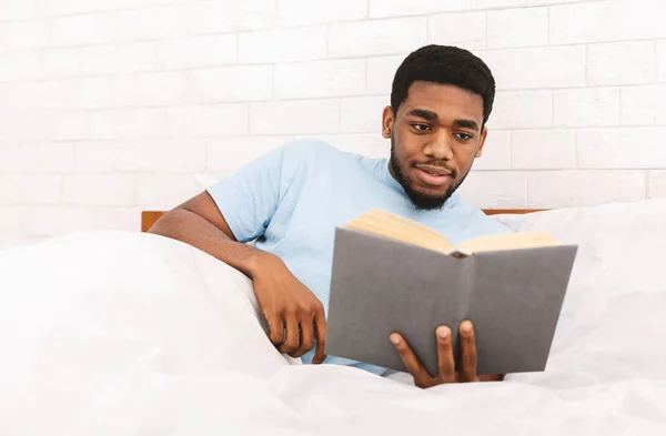 Young black guy reading book in bed — Stock Photo, Image