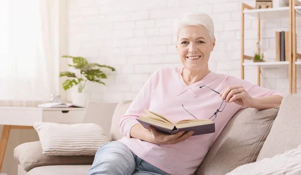 Улыбающаяся пожилая женщина читает книгу дома — стоковое фото