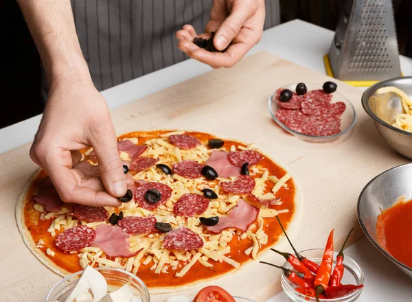 Pizza-Kunst. Chef fügt der Pizza Oliven hinzu — Stockfoto