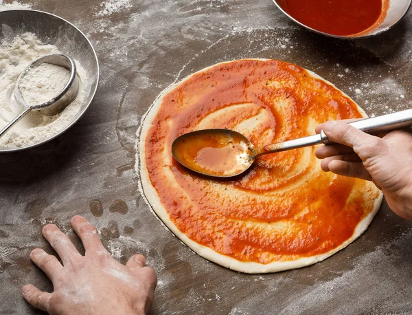 Человек, разбрасывающий томатную пасту на базе пиццы — стоковое фото