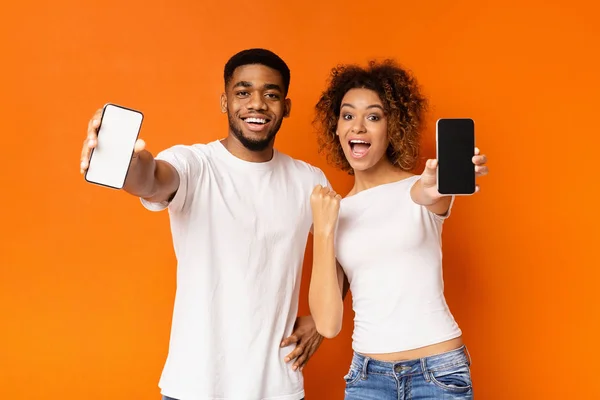 Alegre casal preto mostrando smartphones em branco na câmera — Fotografia de Stock