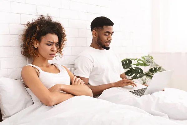 Addicted young man in bed with laptop, woman looking angry — Stock Photo, Image