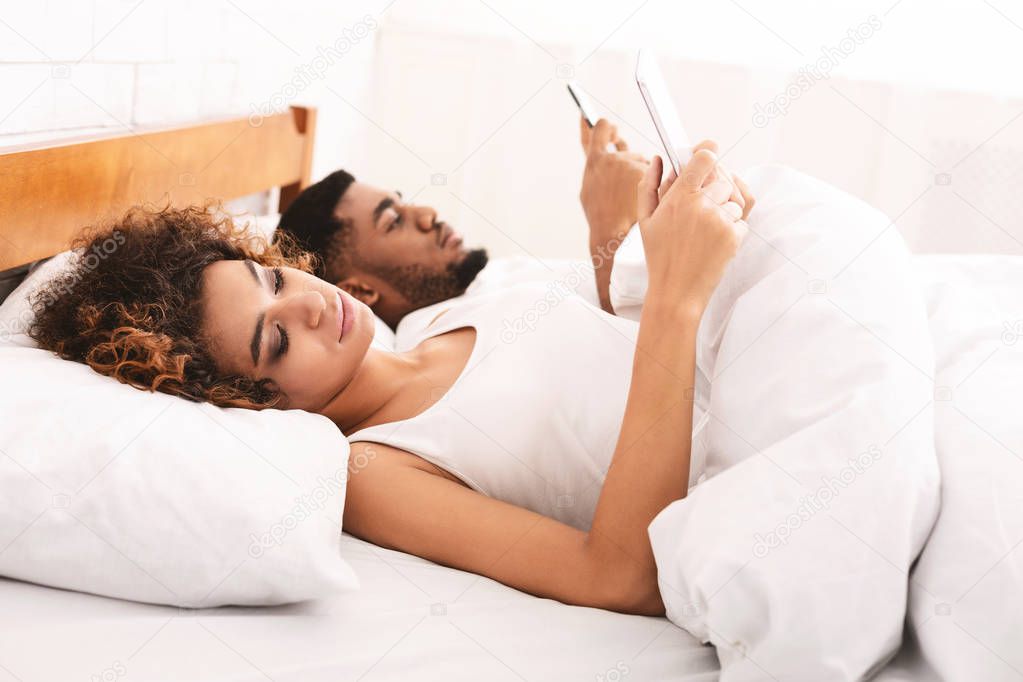 Young couple with mobile phones working from bed