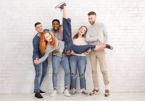 Students holding friend and having fun over brick wall — Stock Photo, Image