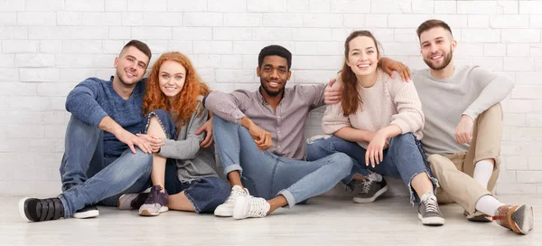 Diverse friends hugging, sitting on floor over light wall — Stock Photo, Image