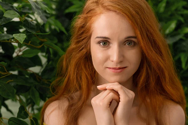 Menina ruiva jovem olhando para a câmera, verde folhas fundo — Fotografia de Stock