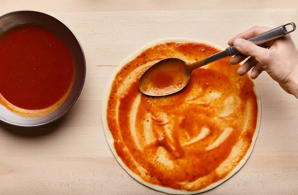 Man spreading tomato paste on pizza base — Stock Photo, Image