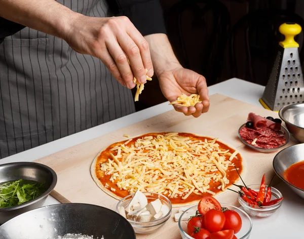 Man sprinkling pizza with cheese at kitchen — Stock Photo, Image