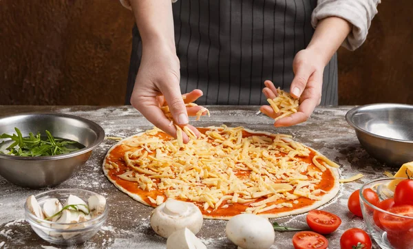 Koch würzt Pizza in der Küche mit Käse — Stockfoto