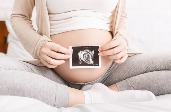 Беременная женщина держит ультразвуковое фото возле живота — стоковое фото