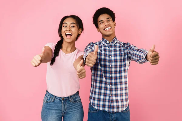 Feliz casal adolescente mostrando polegares para cima, fundo rosa — Fotografia de Stock