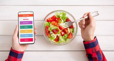 Günlük menü ve yeme salatası ile akıllı telefon kullanan adam