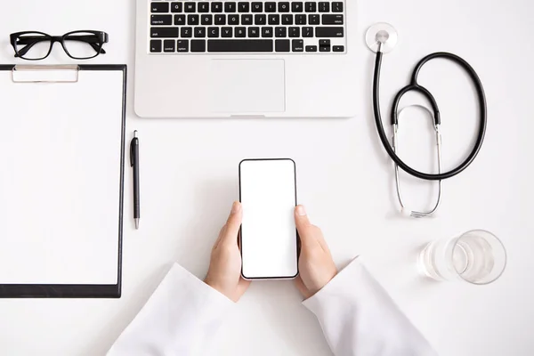 Médico usando smartphone com tela em branco no local de trabalho — Fotografia de Stock