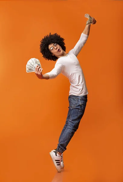 Young excited black man dancing with dollars