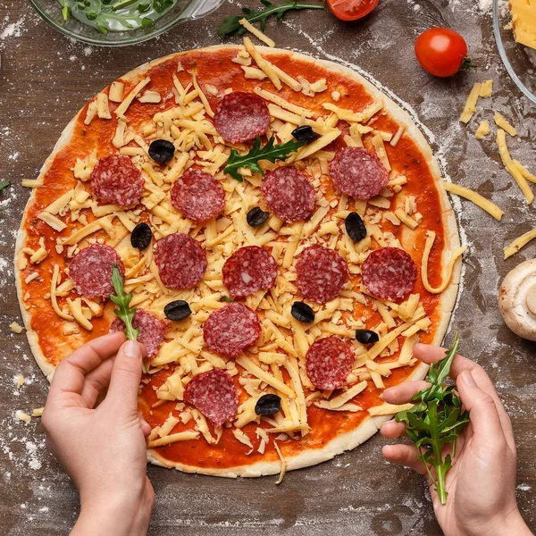 Pizza zubereiten. Frau würzt Pizza mit Rucola — Stockfoto