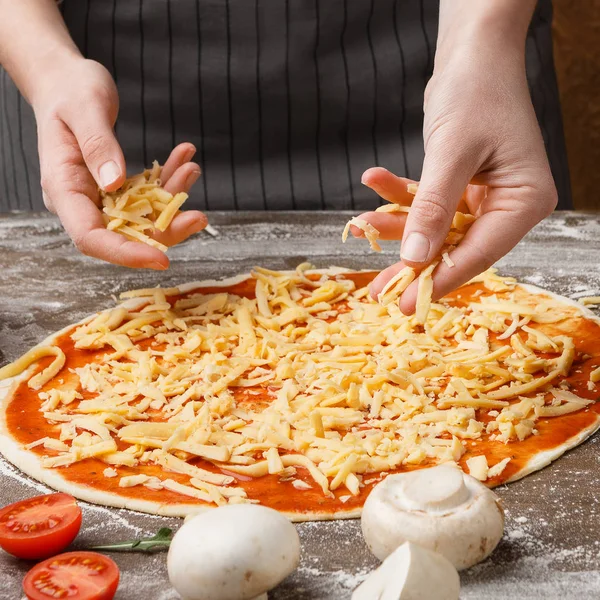 Frau bestreut in Küche Pizza mit Käse — Stockfoto