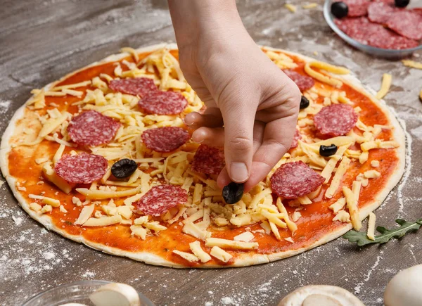 Frau fügt schwarze Oliven zur Pizza hinzu und dekoriert sie — Stockfoto
