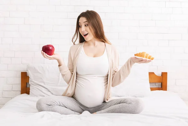 Mulher grávida escolhendo entre croissant e maçã — Fotografia de Stock