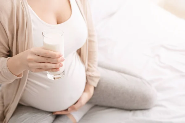 Mladá těhotná žena sedí na posteli s sklenice mléka — Stock fotografie