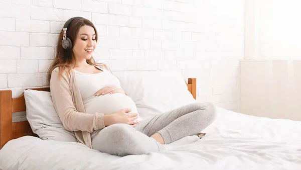 Glückliche junge schwangere Frau hört Musik über Kopfhörer — Stockfoto