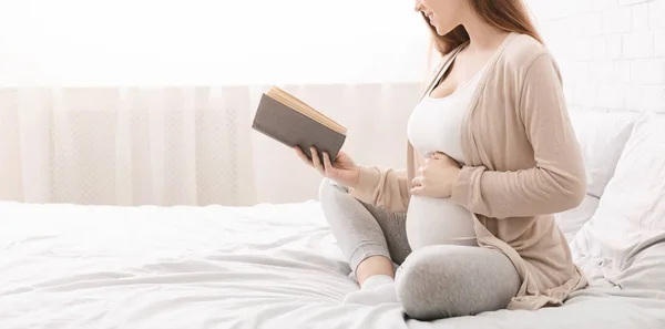 Beautiful pregnant woman reading book on bed