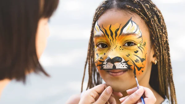 Little girl getting her face painted by face painting artist. — Stock Photo, Image