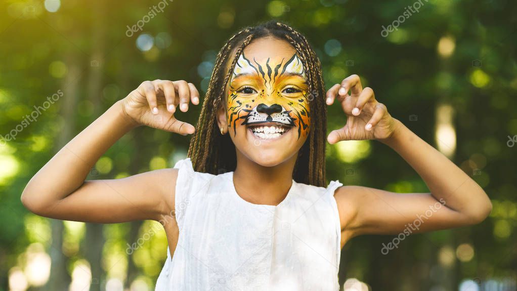 Cheerful little african-american girl with face painting like tiger