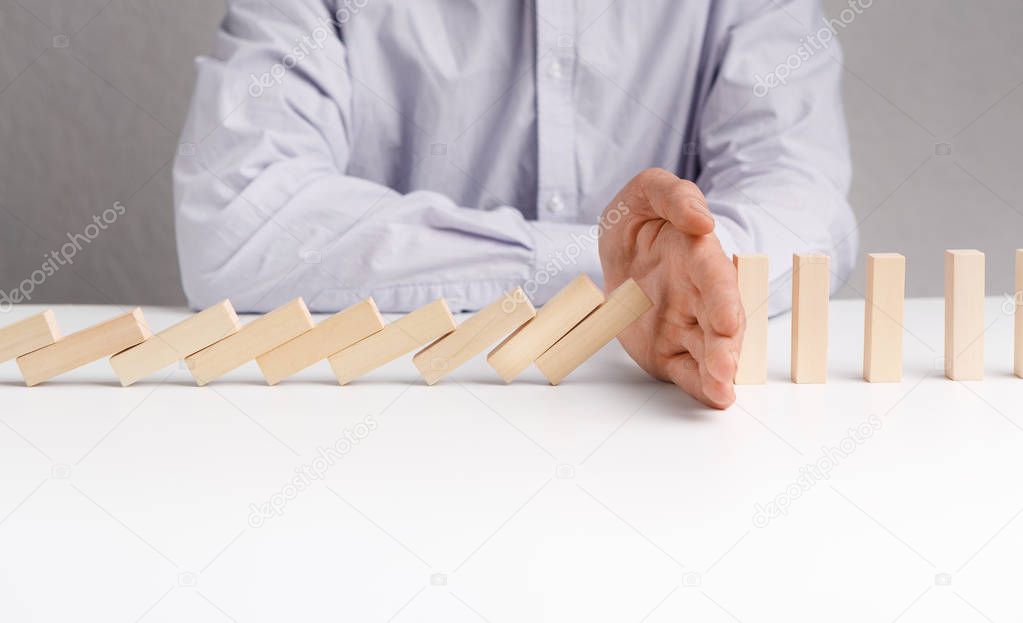 Man stopping domino effect on white table.