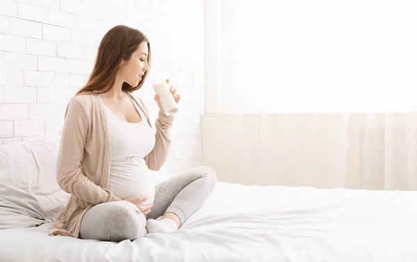 Young pregnant woman sitting on bed with glass of milk — Stock Photo, Image