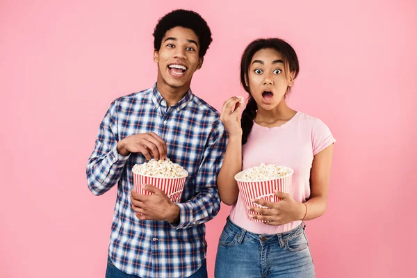 Americký pár jíst popcorn na růžovém pozadí — Stock fotografie