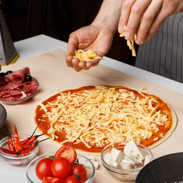 Prozess der Herstellung von Pizza. Koch fügt Käse auf Pizzaboden hinzu — Stockfoto