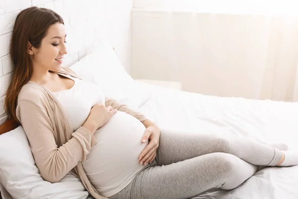 Glada gravida lady smeker hennes mage, liggande i sängen — Stockfoto
