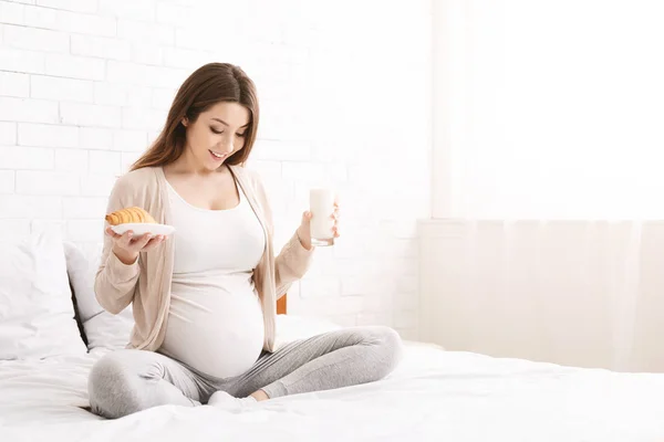 Genç hamile kadın yatağın üstüne oturan brunch sahip — Stok fotoğraf