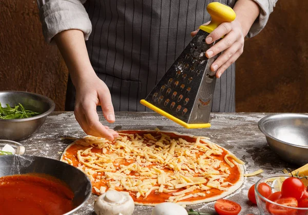 Preparing pizza. Woman rubbing cheese on grater