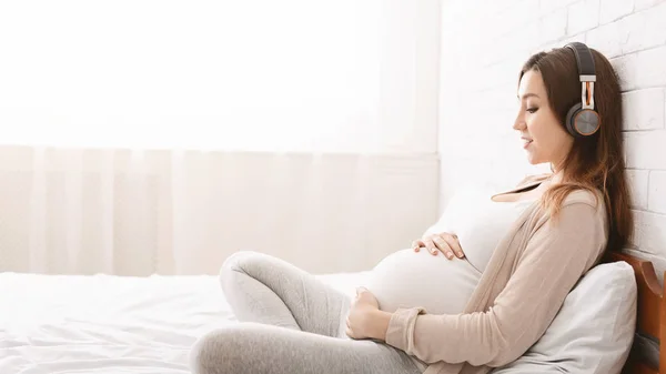 Glad ung gravid kvinna som lyssnar på musik i hörlurar — Stockfoto