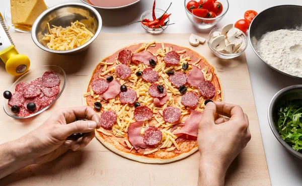 Pizza-Kunst. Mann vermischt Pizza mit Oliven — Stockfoto