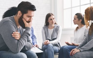 Depressed man sitting at rehab group therapy clipart