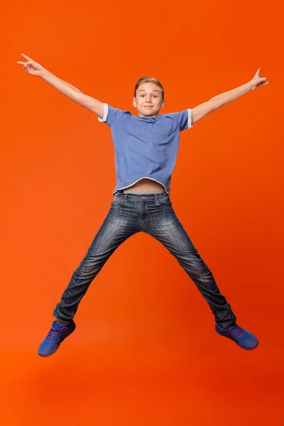 Rapaz feliz pulando no fundo do estúdio laranja — Fotografia de Stock