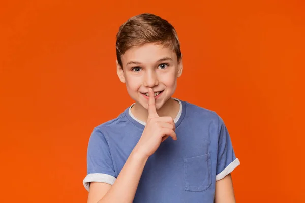 Мальчик показывает знак молчания на оранжевом фоне — стоковое фото
