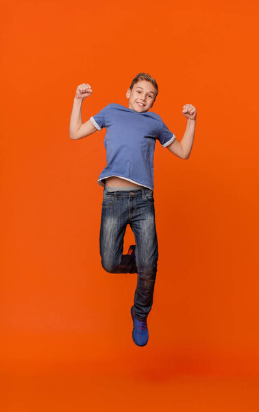 Happy schoolboy jumping for joy on orange